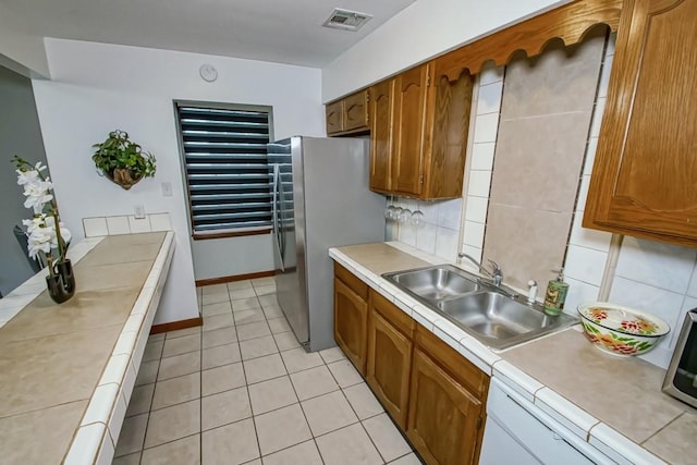 2441 Chartres St, New Orleans, LA 70117 - kitchen with brown cabinetry, visible vents, a sink, light tile patterned floors, and freestanding refrigerator
