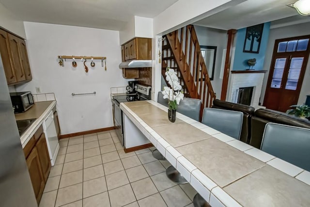 2441 Chartres St, New Orleans, LA 70117 - kitchen with brown cabinetry, dishwasher, stainless steel electric range, under cabinet range hood, and light tile patterned floors