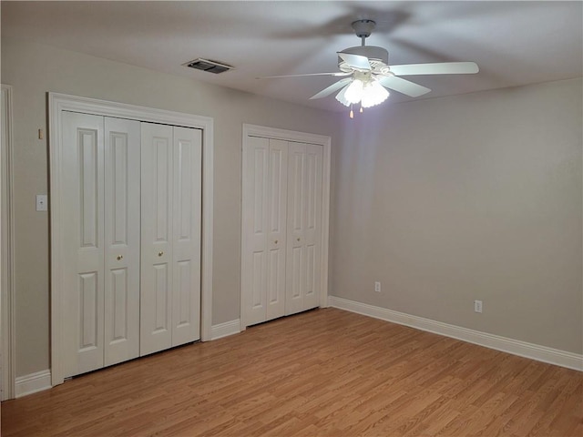 unfurnished bedroom featuring a ceiling fan, visible vents, baseboards, two closets, and light wood-style floors