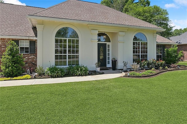 view of front of home with roof with shingles, brick siding, and a front yard