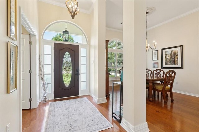foyer entrance with a chandelier, wood finished floors, ornamental molding, and baseboards