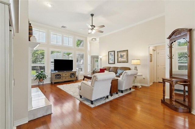 living room featuring ceiling fan, ornamental molding, wood-type flooring, baseboards, and a towering ceiling