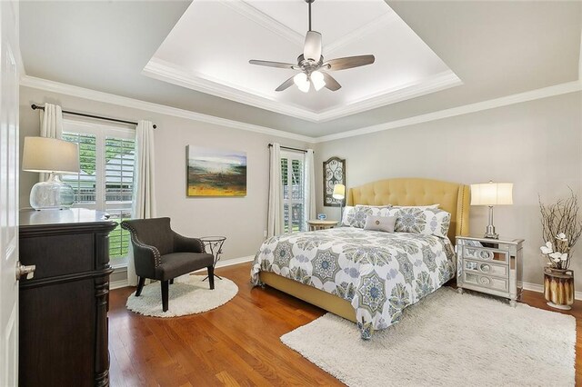 bedroom with a raised ceiling, wood finished floors, baseboards, ornamental molding, and a ceiling fan