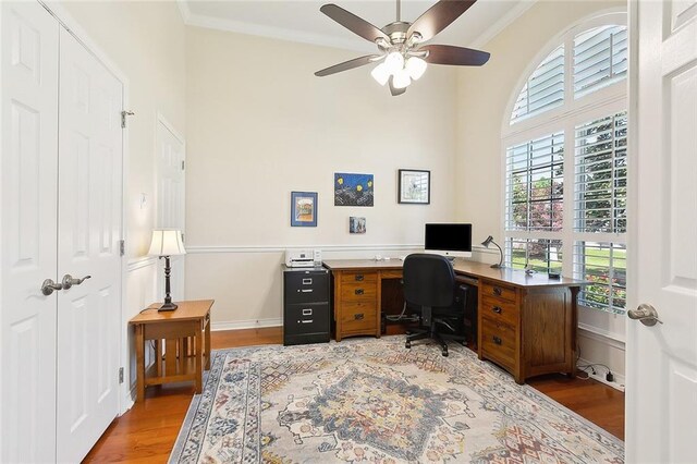 home office with light wood-style floors, a ceiling fan, a towering ceiling, and crown molding