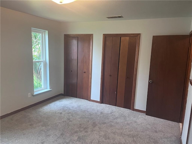 unfurnished bedroom featuring carpet floors, multiple closets, multiple windows, and baseboards