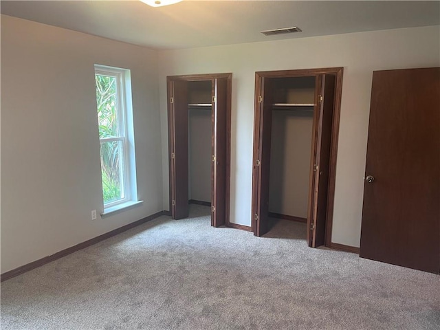 unfurnished bedroom featuring two closets, carpet flooring, multiple windows, and baseboards