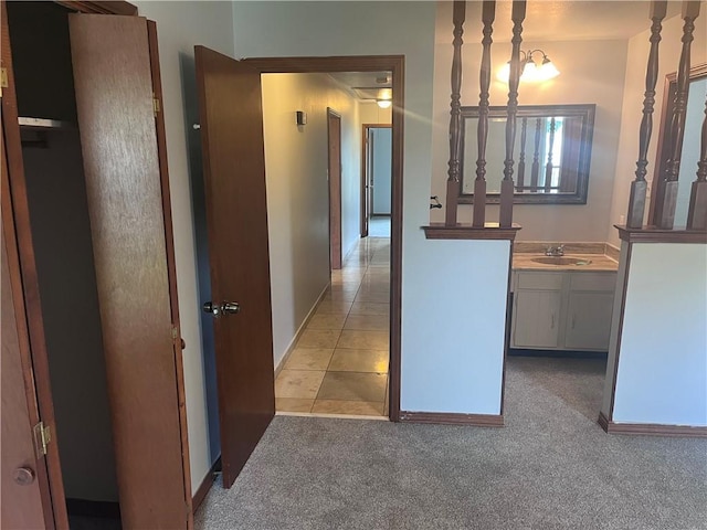 hall featuring a sink, carpet, baseboards, and tile patterned flooring