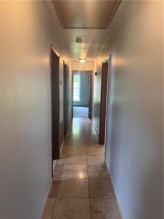 hallway featuring attic access, baseboards, and light tile patterned floors