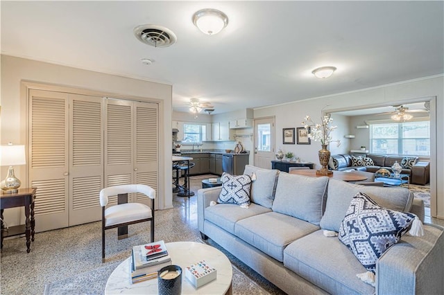 living area featuring light speckled floor, crown molding, ceiling fan, and visible vents