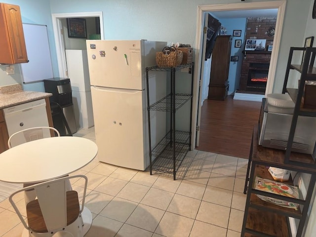 kitchen with light countertops, a brick fireplace, white appliances, and light tile patterned flooring