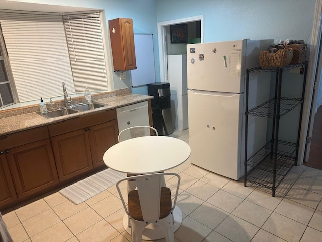 kitchen with brown cabinets, a sink, white appliances, light countertops, and light tile patterned floors