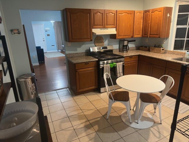 5167 Lafaye St, New Orleans, LA 70122 - kitchen featuring stainless steel gas range, under cabinet range hood, brown cabinetry, light stone countertops, and light tile patterned flooring