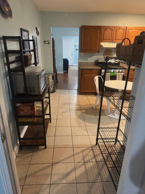 kitchen featuring stainless steel range with gas cooktop, brown cabinetry, under cabinet range hood, and light tile patterned floors