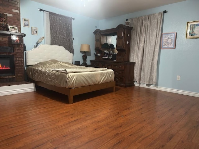 bedroom with a brick fireplace, baseboards, and wood finished floors