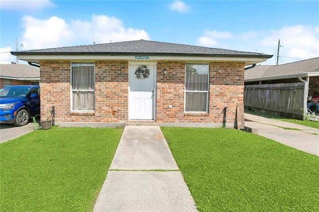 bungalow with brick siding, a shingled roof, fence, and a front yard