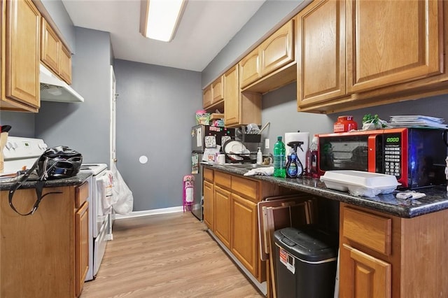 kitchen featuring white range with electric cooktop, light wood-style flooring, dark stone countertops, freestanding refrigerator, and under cabinet range hood