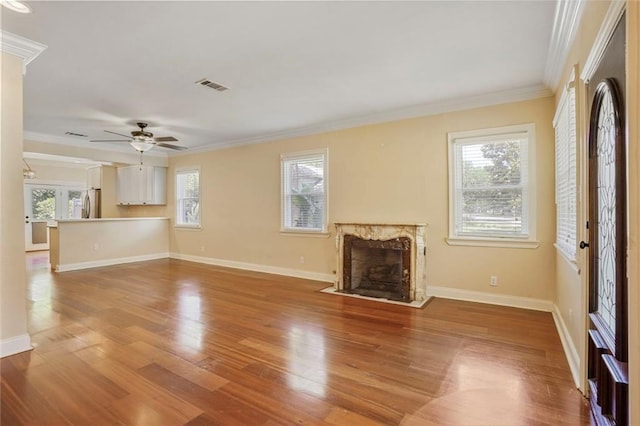 unfurnished living room featuring a fireplace, baseboards, wood finished floors, visible vents, and ornamental molding