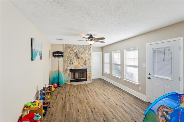 2967 Camellia Dr, Slidell, LA 70458 - unfurnished living room featuring wood finished floors, a stone fireplace, baseboards, ceiling fan, and a textured ceiling