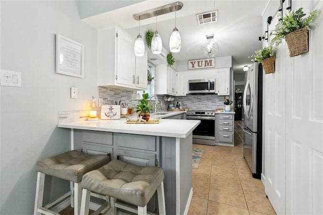 kitchen featuring visible vents, tasteful backsplash, a sink, a peninsula, and stainless steel appliances