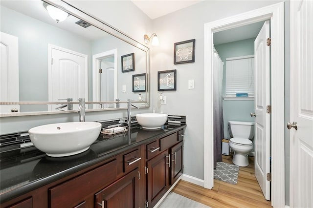 bathroom with double vanity, visible vents, wood finished floors, a sink, and toilet