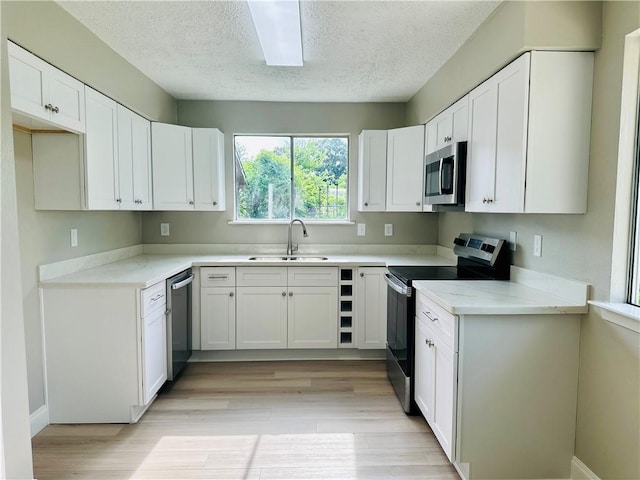 kitchen featuring a sink, a textured ceiling, light wood-style flooring, stainless steel appliances, and white cabinetry