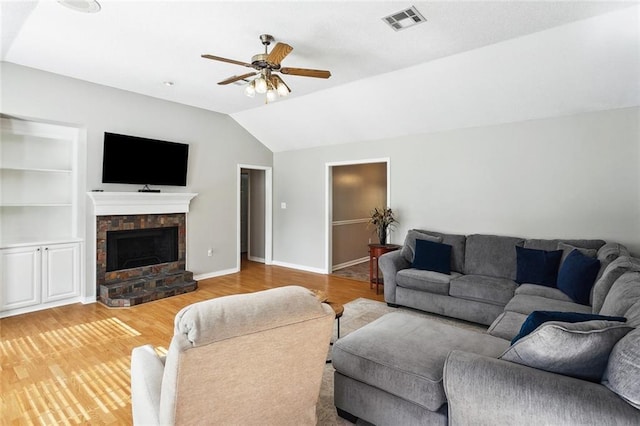 living area featuring ceiling fan, a stone fireplace, visible vents, light wood finished floors, and lofted ceiling