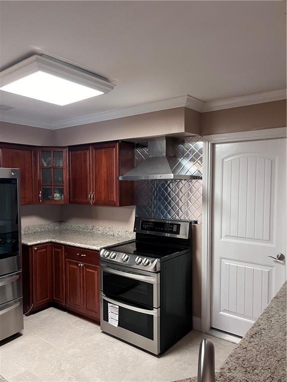 kitchen featuring decorative backsplash, crown molding, appliances with stainless steel finishes, glass insert cabinets, and wall chimney exhaust hood