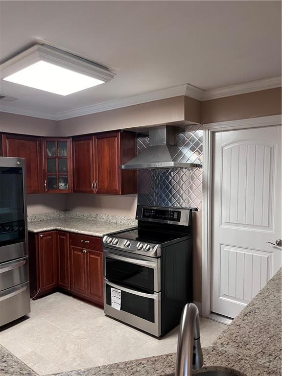 kitchen featuring wall chimney range hood, crown molding, stainless steel appliances, visible vents, and glass insert cabinets