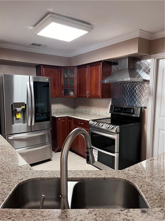 kitchen with wall chimney range hood, crown molding, a sink, stainless steel appliances, and glass insert cabinets