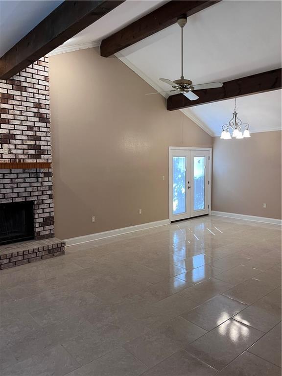 unfurnished living room featuring tile patterned flooring, a brick fireplace, baseboards, ceiling fan with notable chandelier, and vaulted ceiling with beams