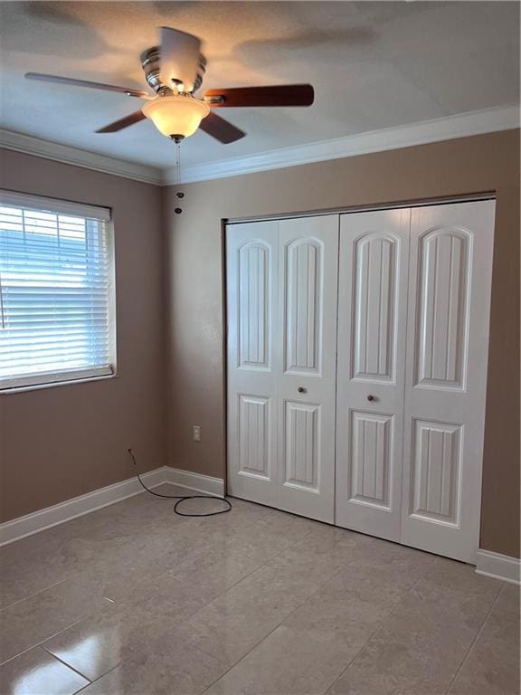 unfurnished bedroom with crown molding, baseboards, ceiling fan, and a closet