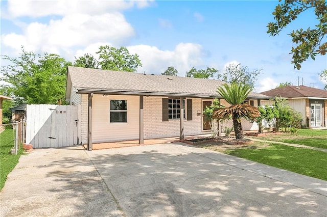single story home featuring a gate, brick siding, fence, a front lawn, and concrete driveway