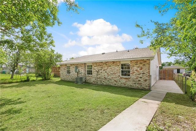 rear view of house with a lawn, fence, central air condition unit, and brick siding