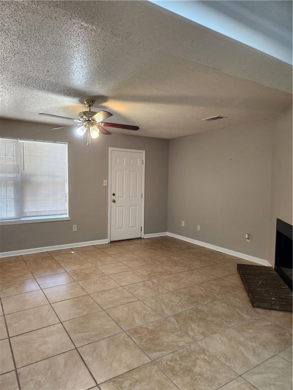 unfurnished living room with visible vents, baseboards, a textured ceiling, a ceiling fan, and light tile patterned floors