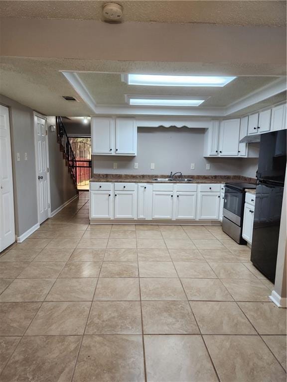 kitchen with a textured ceiling, a sink, white cabinets, freestanding refrigerator, and electric stove