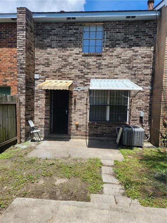 view of front facade featuring fence, central AC unit, a patio, and brick siding