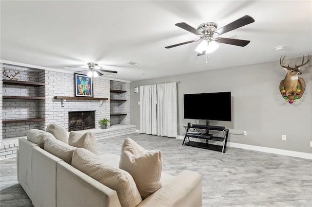 living room featuring a ceiling fan, a brick fireplace, built in shelves, wood finished floors, and baseboards