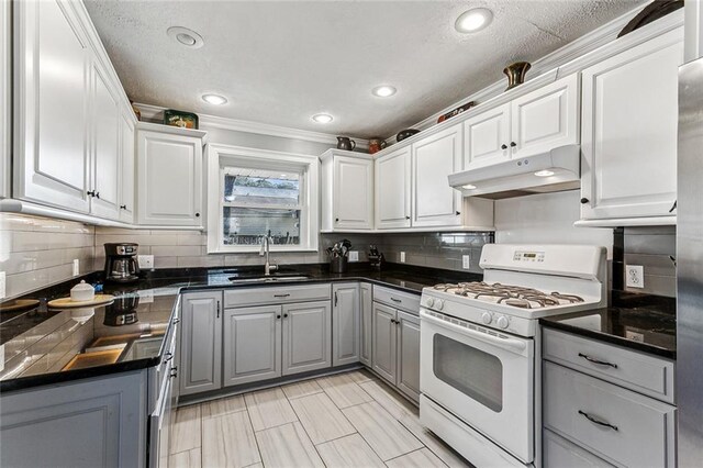 kitchen featuring dark countertops, a sink, gray cabinetry, white range with gas cooktop, and under cabinet range hood
