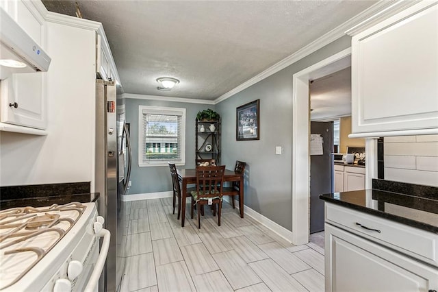 kitchen with crown molding, gas range gas stove, baseboards, white cabinets, and under cabinet range hood