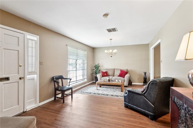 living area with baseboards, an inviting chandelier, wood finished floors, and visible vents
