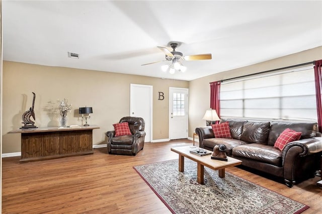 living room featuring visible vents, a ceiling fan, baseboards, and wood finished floors
