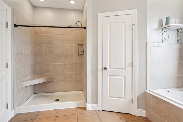 bathroom featuring a relaxing tiled tub, tile patterned floors, a tile shower, and baseboards