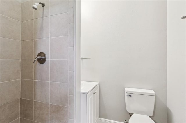 bathroom with toilet, tiled shower, and vanity