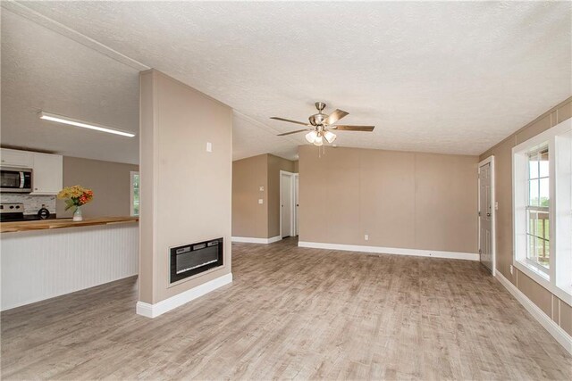 32536 D Wascom Rd, Mount Hermon, LA 70450 - unfurnished living room featuring light wood finished floors, a textured ceiling, a glass covered fireplace, a ceiling fan, and baseboards