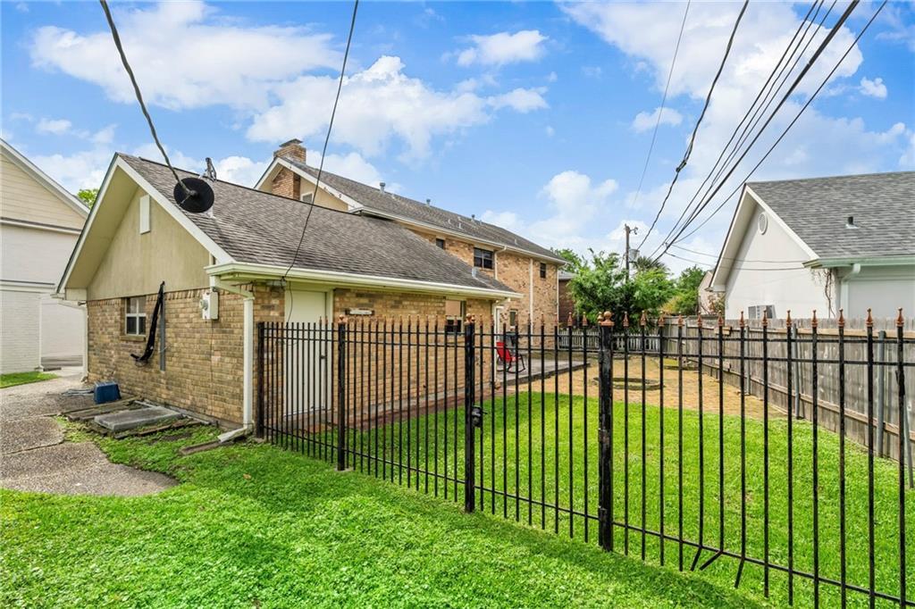 back of house with a lawn, brick siding, fence private yard, and roof with shingles