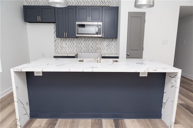 271719 Clover St, New Orleans, LA 70122 - kitchen featuring stainless steel microwave, an island with sink, light stone counters, tasteful backsplash, and light wood finished floors
