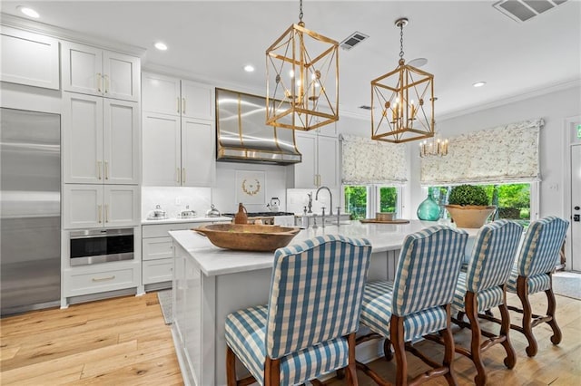 34 Riverdale Dr, Covington, LA 70433 - kitchen featuring ventilation hood, a chandelier, crown molding, light countertops, and a kitchen island with sink