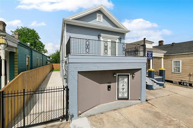 shotgun-style home featuring brick siding, a gate, fence, and a balcony