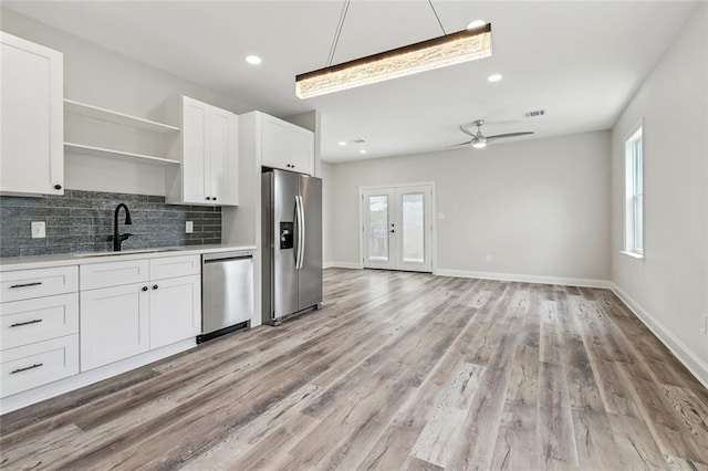 kitchen with decorative backsplash, open shelves, a sink, light countertops, and stainless steel appliances
