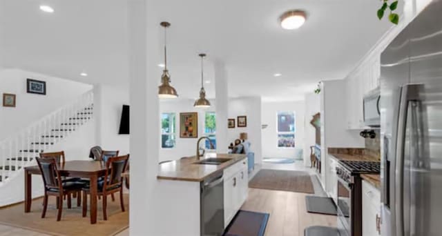 542 Abalon Ct, New Orleans, LA 70114 - kitchen featuring stainless steel appliances, a sink, white cabinets, light wood-style floors, and pendant lighting